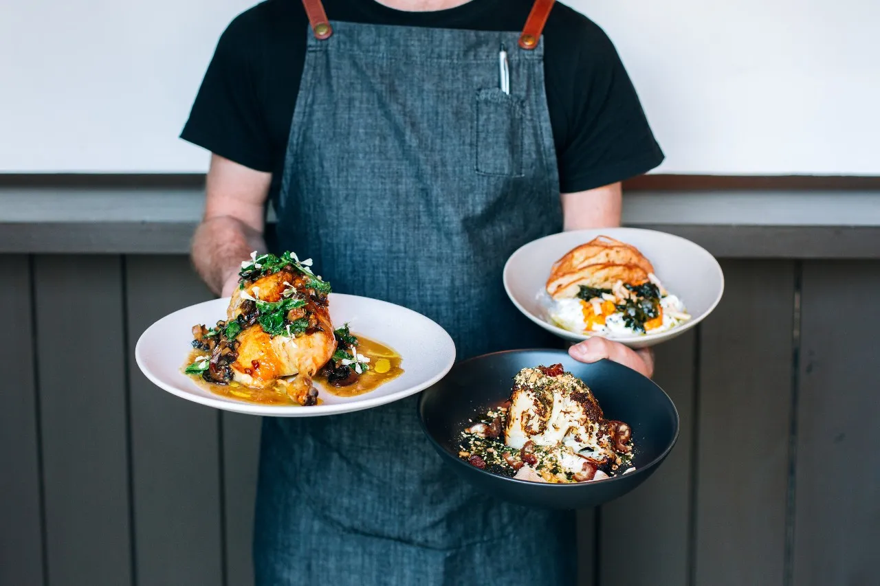A waiter at Kika restaurant in Wanaka holding three plates.